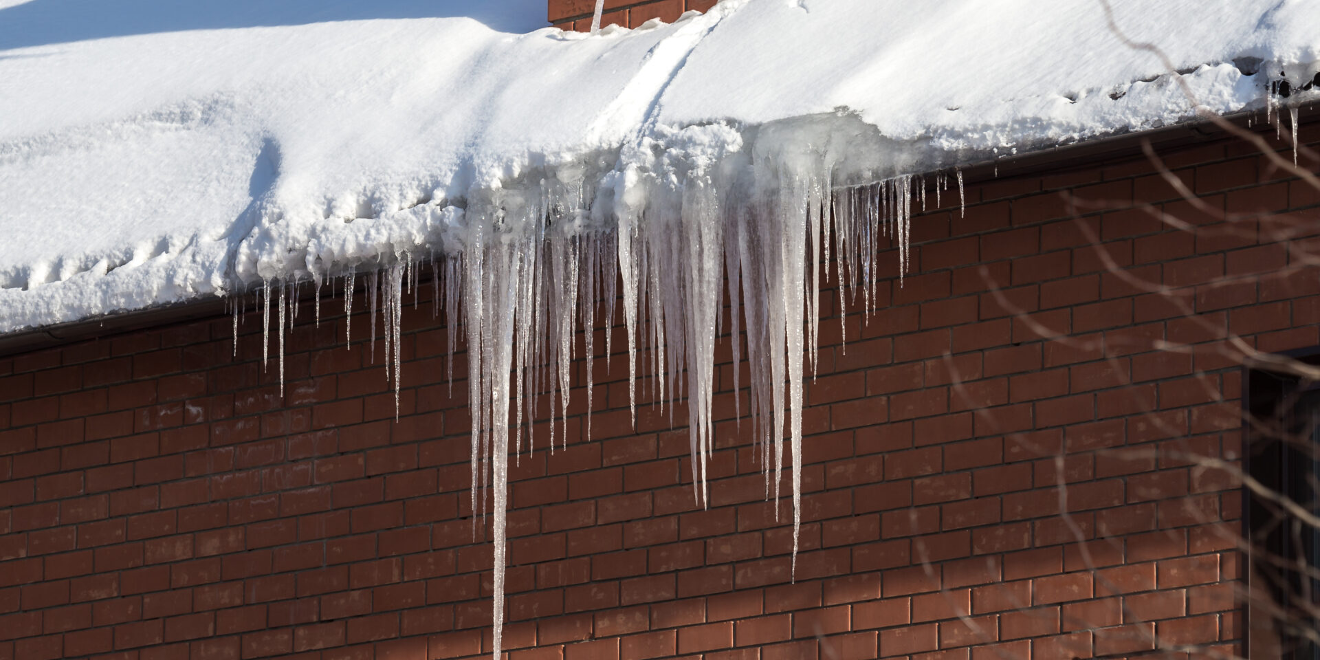 Large,Icicles,Hanging,From,The,Roof,Of,A,Brick,House
